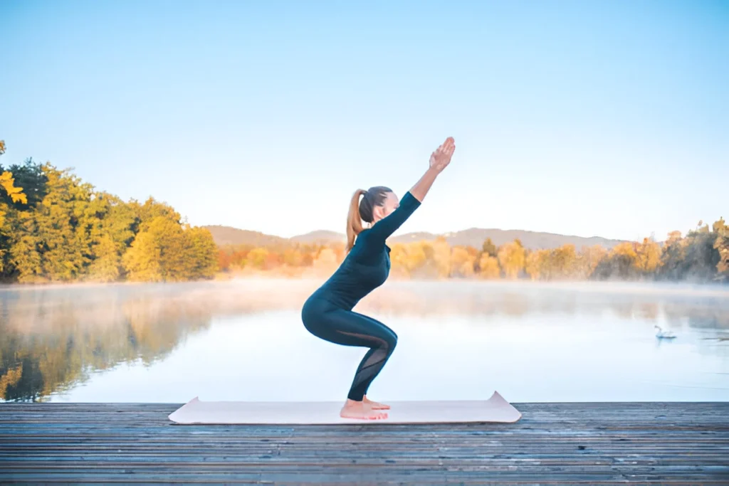 A person holding Utkatasana (Chair Pose) with knees bent and arms raised overhead.